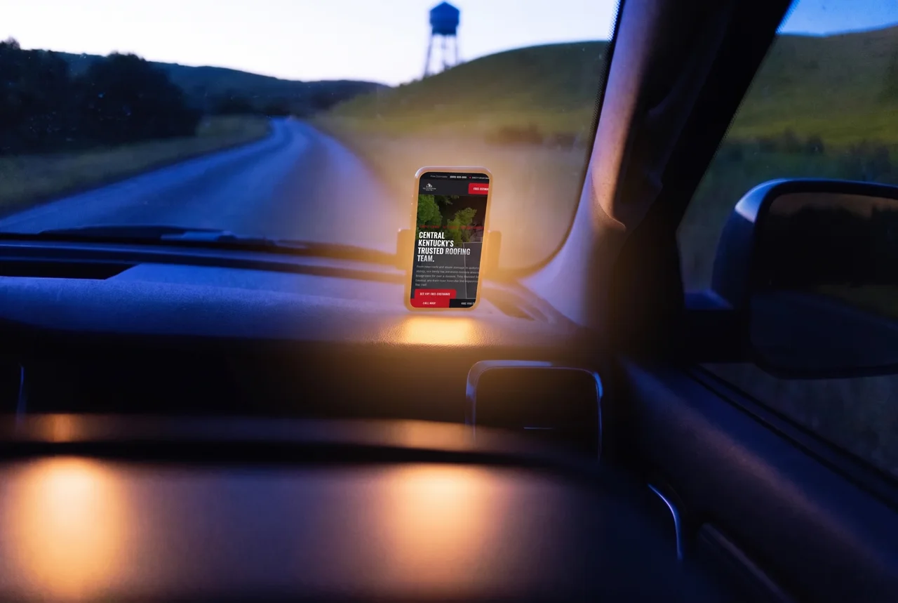 A phone in a dashboard mount inside a pickup cab on a two-lane road at dusk, hills and a distant water tower through the windshield.