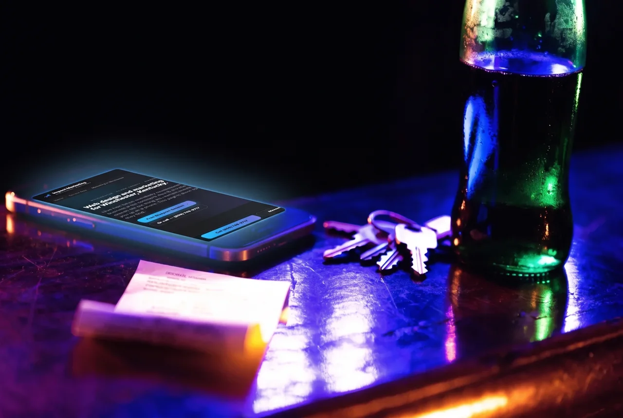 A phone, a receipt and a set of keys on a wooden shop counter beside a green glass soda bottle, evening light.